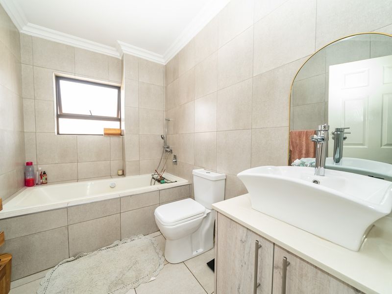 Modern bathroom featuring a built-in bathtub, vessel sink with vanity cabinet, and neutral floor-to-ceiling tiling.