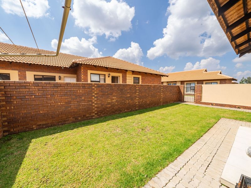 A private rear garden featuring a well-maintained lawn, paved pathway, and secure brick boundary walls, providing a functional outdoor space for the townhouse.