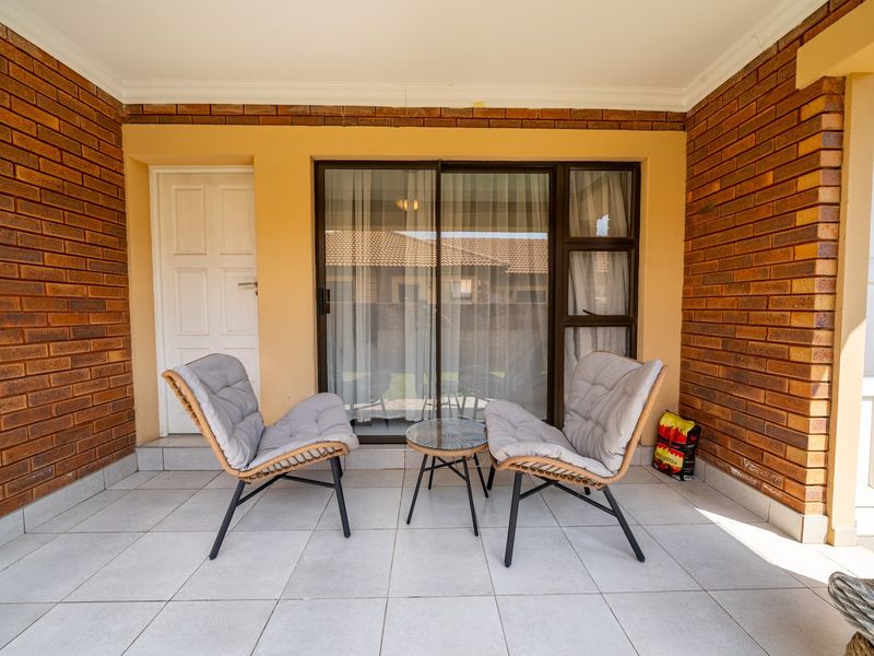 A covered patio area featuring exposed brick walls, tiled flooring, and a sliding glass door providing access to the interior.