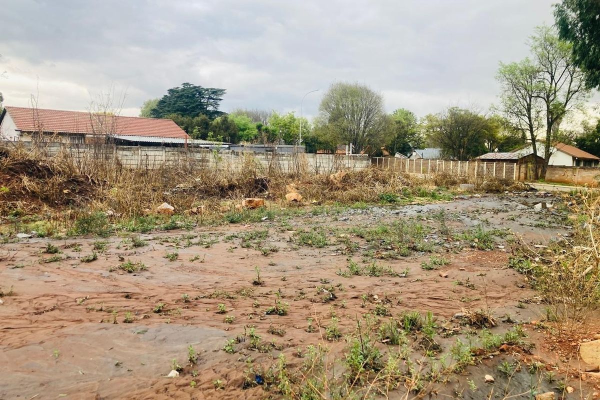 A vacant residential plot featuring uneven terrain, overgrown vegetation, and existing perimeter boundary walls.