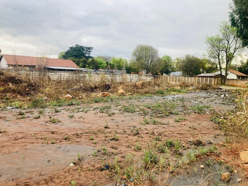 A vacant residential plot featuring uneven terrain, overgrown vegetation, and existing perimeter boundary walls.