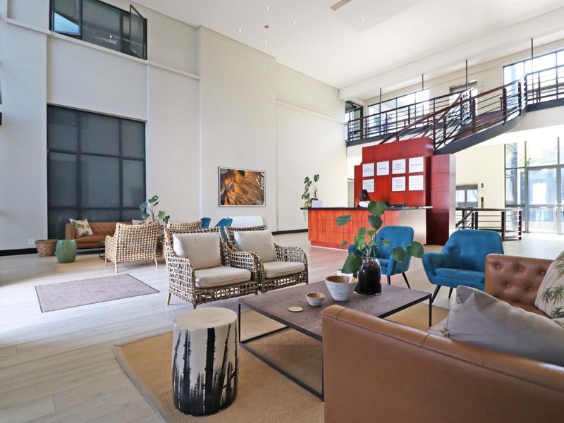 Spacious open-plan office reception area featuring high ceilings, a built-in reception desk, a mezzanine level with a staircase, and large windows.