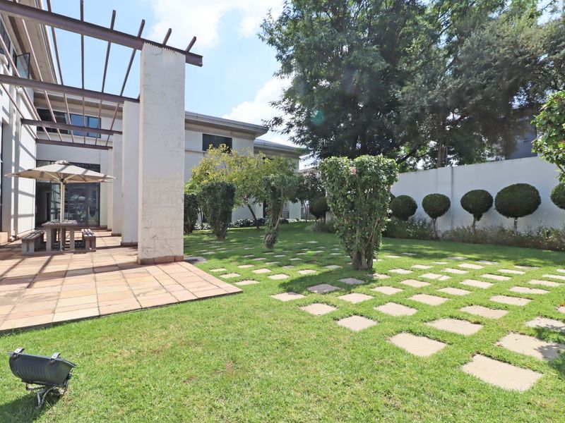 A spacious rear garden featuring a tiled patio area with a pergola, well-maintained lawn, and structured landscaping along the boundary wall.