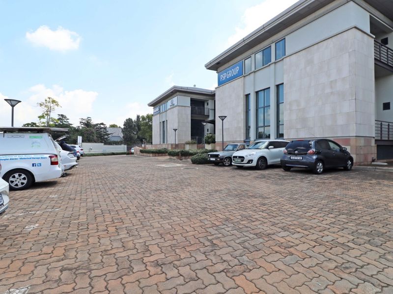 Exterior view of a modern office building featuring stone facade cladding, large windows, and a paved parking area.