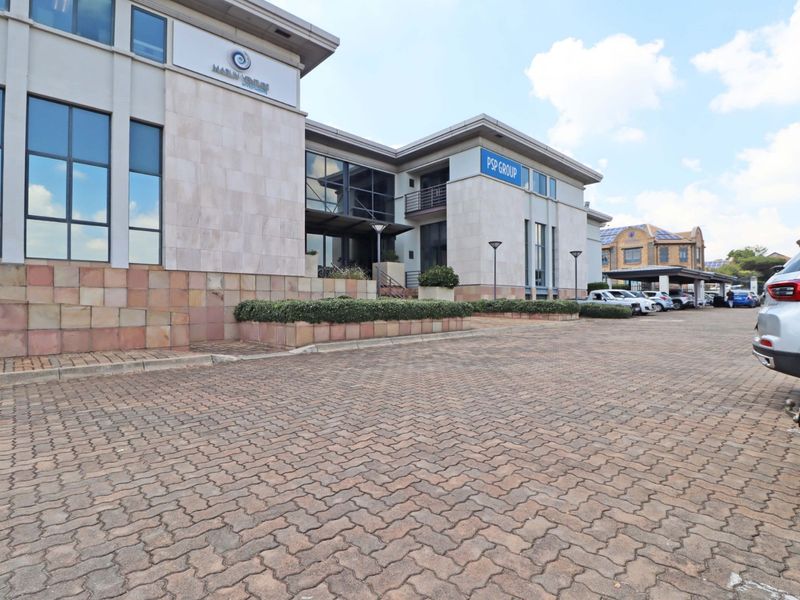 Front exterior view of a modern multi-story office building featuring stone cladding, large glass windows, and a paved parking area.