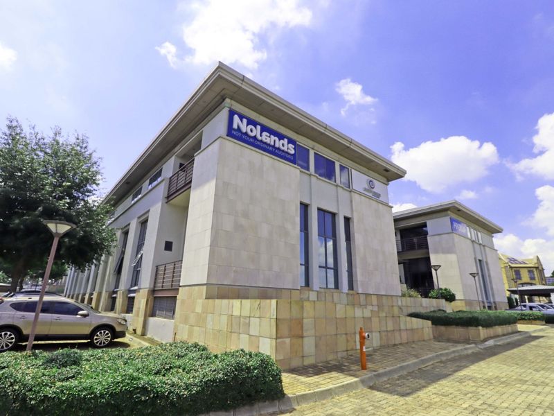 A modern multi-story office building featuring stone facade cladding, balconies, and paved exterior grounds with dedicated parking.