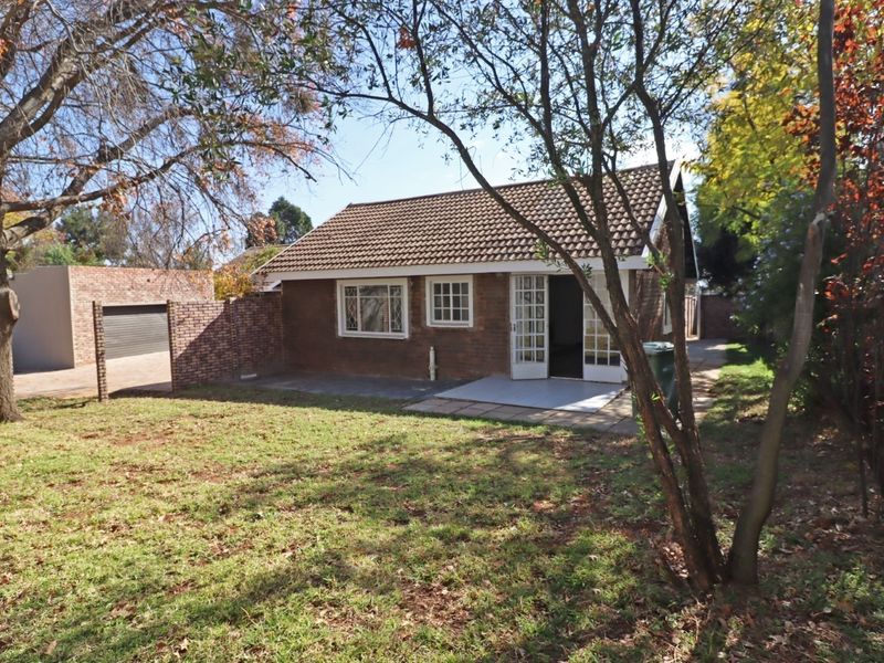 Rear view of a brick-built property featuring a tiled roof, paved patio area, and access via french doors, set within a private garden.