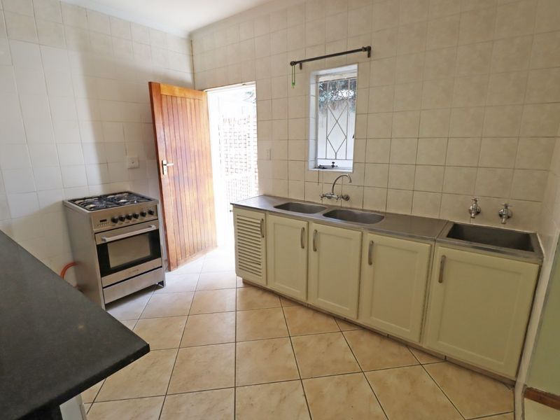 A functional kitchen featuring tiled walls and flooring, a gas stove, and a stainless steel double sink with built-in cabinetry.