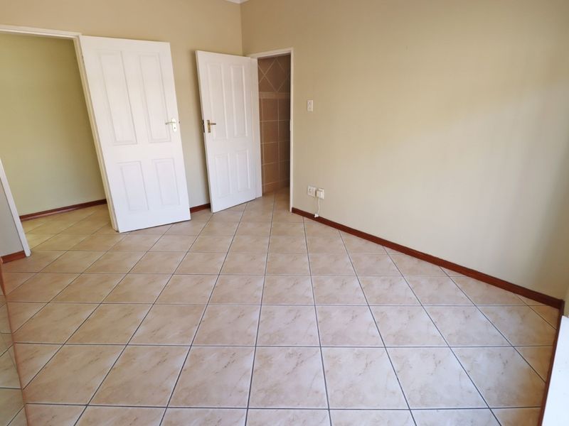 An empty bedroom featuring neutral wall paint, tiled flooring, and two white panel doors leading to adjacent spaces.
