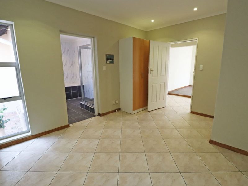 A spacious, neutral bedroom featuring tiled flooring, recessed lighting, and direct access to an en-suite bathroom.