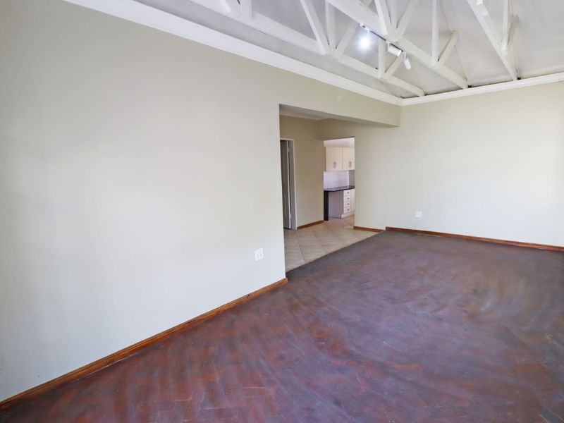 Spacious open-plan living area featuring exposed white roof trusses, herringbone parquet flooring, and a view through to the kitchen area.
