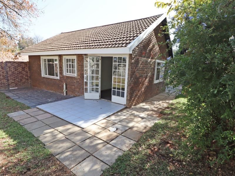 Rear view of a brick building featuring a paved patio area, french doors, and a tiled roof, set within a garden space.