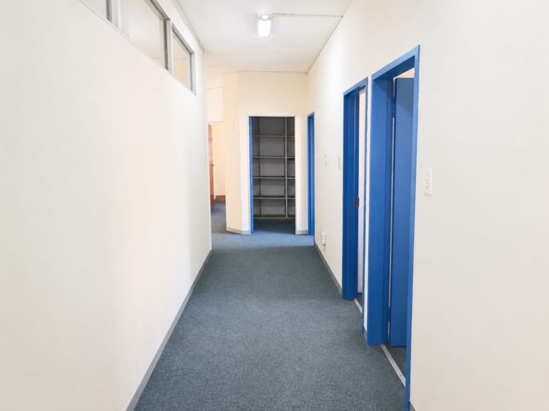A functional office hallway featuring blue door frames, carpeted flooring, and built-in shelving units at the end of the corridor.
