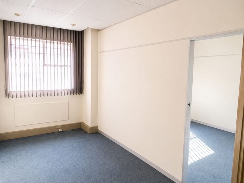 A vacant office space featuring neutral walls, blue carpet flooring, a suspended ceiling, and vertical blinds on the window.