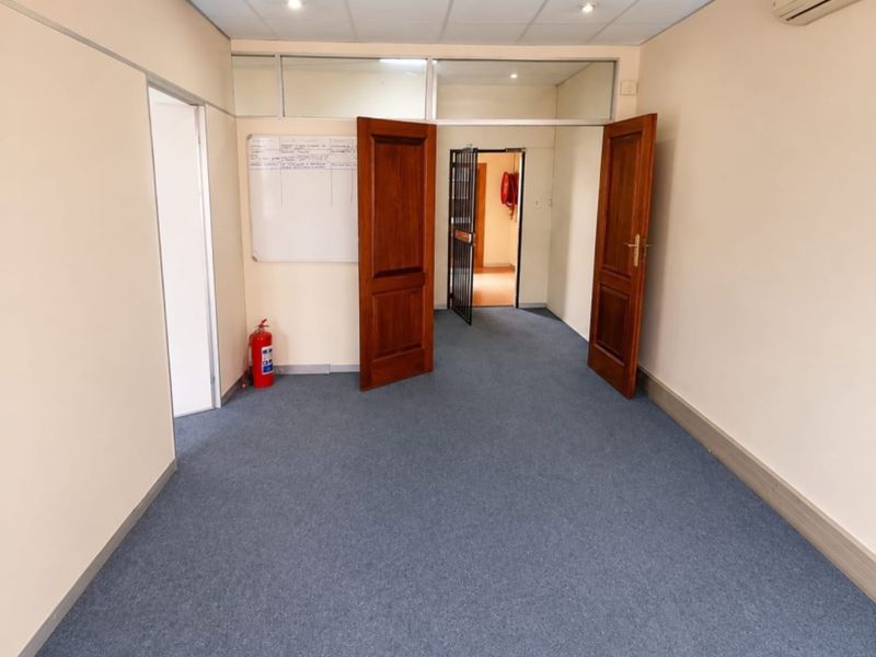 A clean, empty office space featuring carpeted flooring, a suspended ceiling with recessed lighting, and a secure entry point with timber doors.