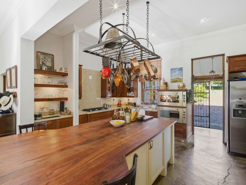 Spacious farmhouse kitchen featuring a large wooden island, hanging pot rack, built-in oven, gas hob, and open shelving with direct access to the exterior.