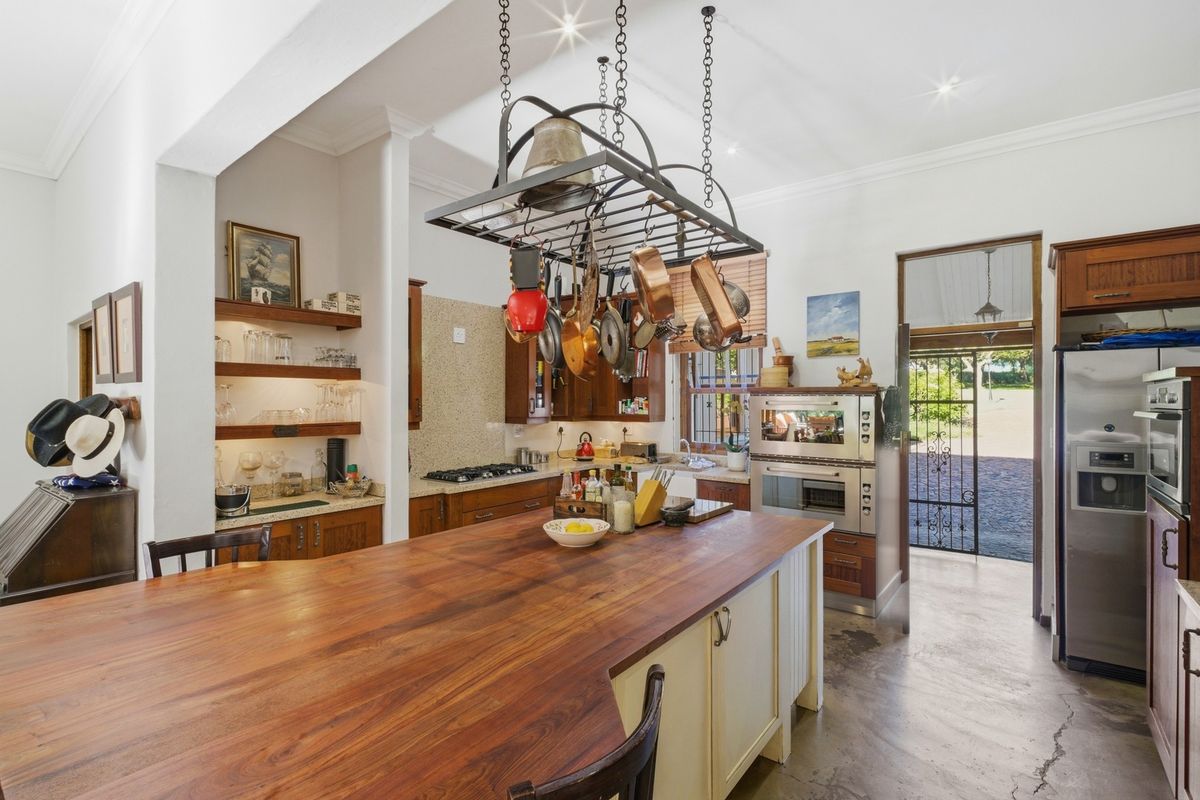 Spacious farmhouse kitchen featuring a large wooden island, hanging pot rack, built-in oven, gas hob, and open shelving with direct access to the exterior.