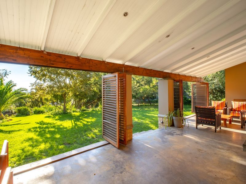 A spacious covered patio featuring timber beam ceilings, recessed lighting, and folding timber shutters, opening directly onto a lush green garden.