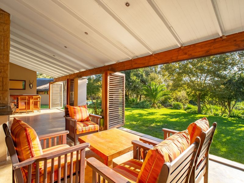 Spacious covered patio featuring a built-in bar area, timber beams, and louvered shutters, overlooking a lush green garden.