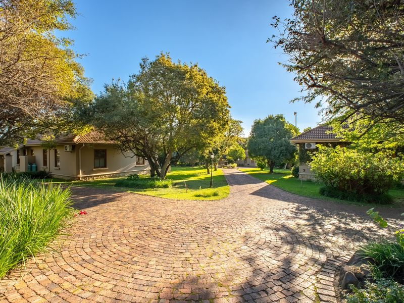 A well-maintained farm property featuring a circular cobblestone driveway, mature trees, and established garden surroundings with multiple building structures.