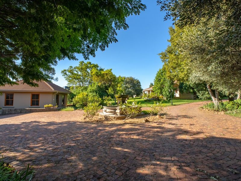 A beautifully landscaped farm courtyard featuring a central stone fountain, brick paving, and mature trees surrounding the main residence.