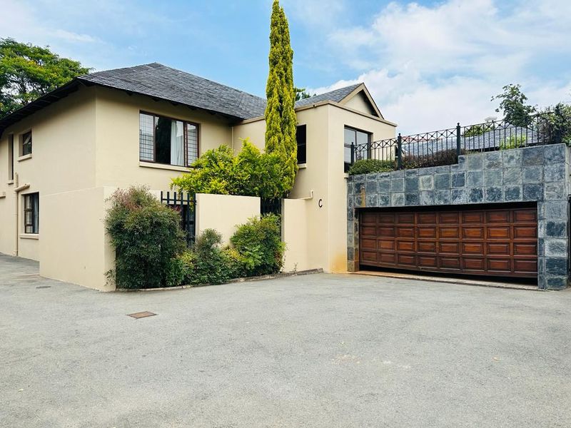 Front elevation of a townhouse featuring a double garage with wooden doors, stone cladding accents, and a paved driveway.