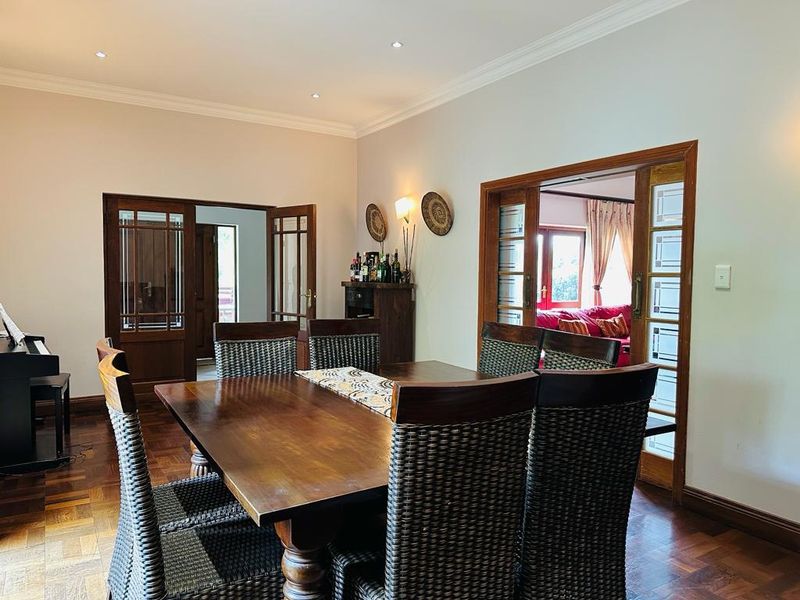 Spacious dining room featuring classic parquet flooring, elegant timber-framed glass doors, and recessed lighting, creating a warm and inviting atmosphere for formal meals.