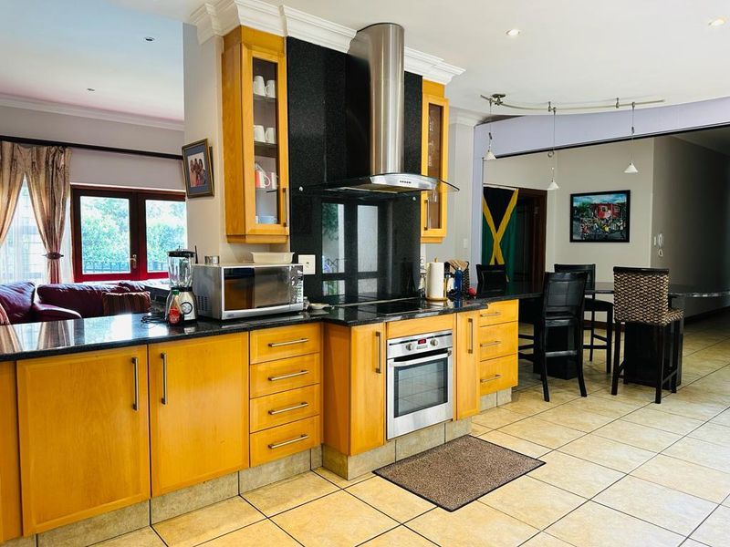 Open-plan kitchen featuring wooden cabinetry, granite countertops, and integrated stainless steel appliances, seamlessly flowing into the adjacent dining and living areas.