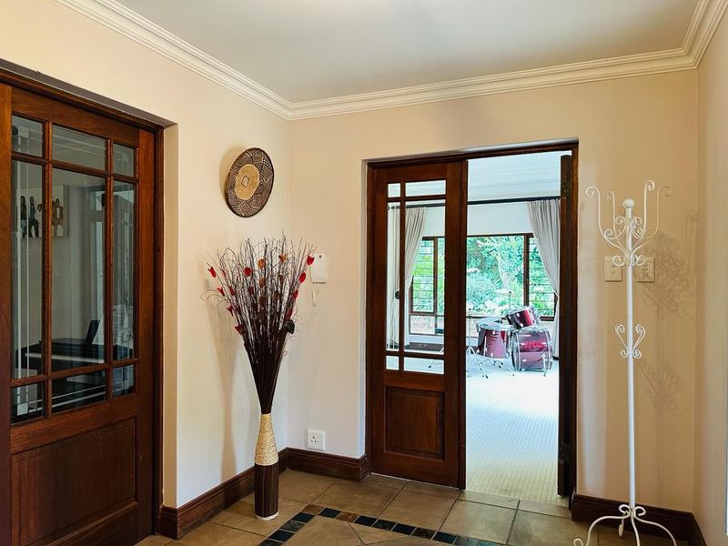 A welcoming entrance hall featuring classic wooden framed glass doors, tiled flooring, and elegant coving, providing a bright transition into the home.