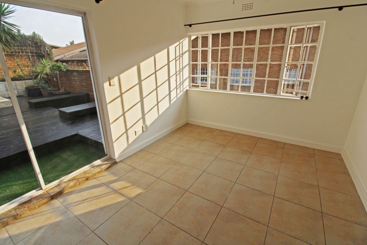 An empty living room featuring tiled flooring, a large grid-pattern window, and a sliding glass door providing direct access to an outdoor patio area.