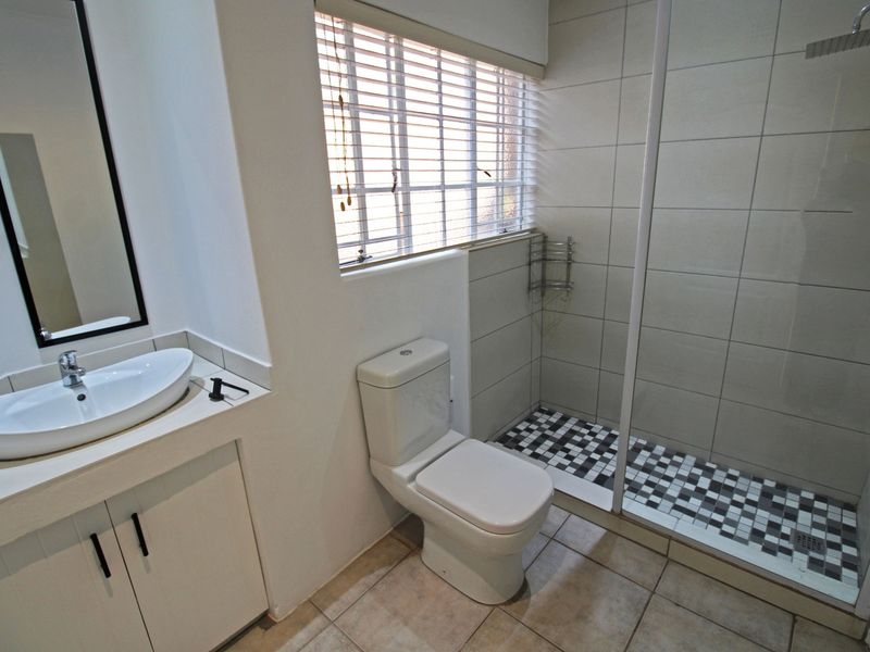 A clean, modern bathroom featuring a vessel sink vanity, a toilet, and a walk-in shower with a rain shower head and decorative tiled flooring.