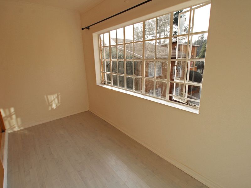 An empty bedroom featuring light-toned laminate flooring, a large steel-framed window, and a built-in cupboard.