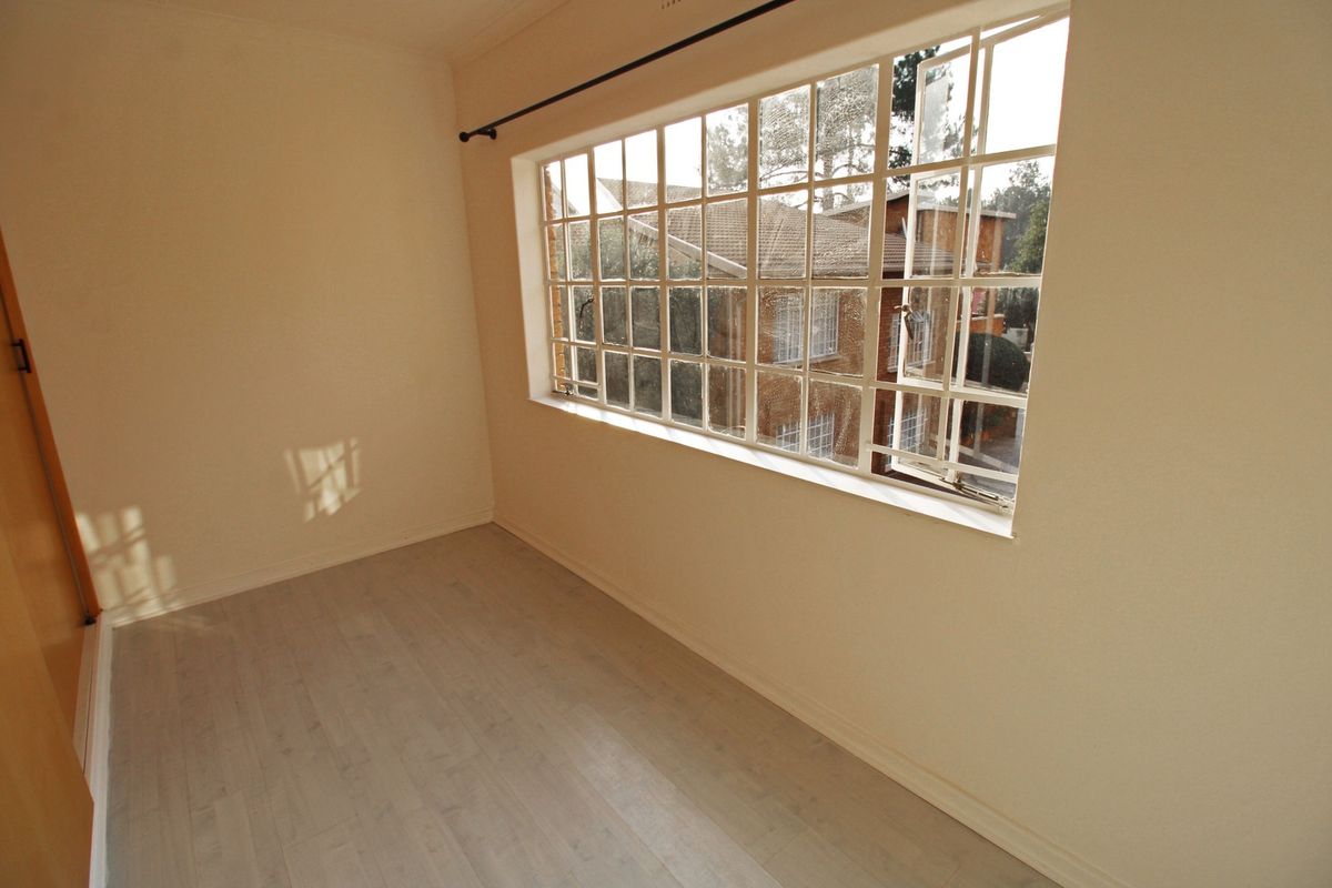 An empty bedroom featuring light-toned laminate flooring, a large steel-framed window, and a built-in cupboard.