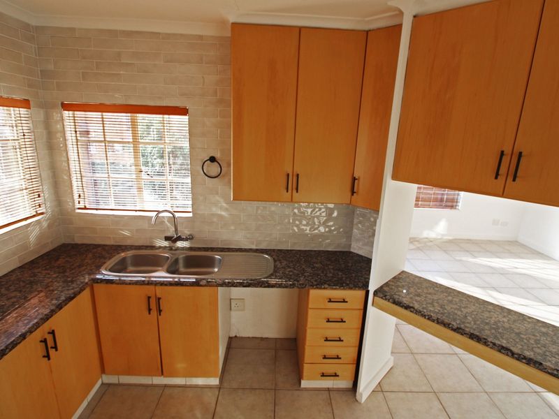 A functional kitchen featuring light wood cabinetry, granite countertops, a double sink, and a breakfast bar overlooking the adjacent living area.