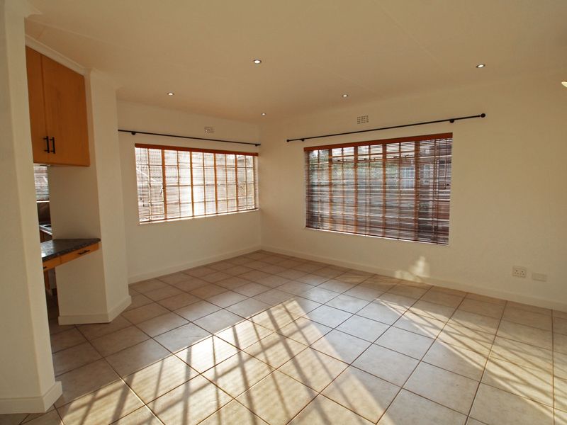 Bright and spacious open-plan living area featuring neutral tiled flooring, recessed lighting, and large windows with fitted venetian blinds.