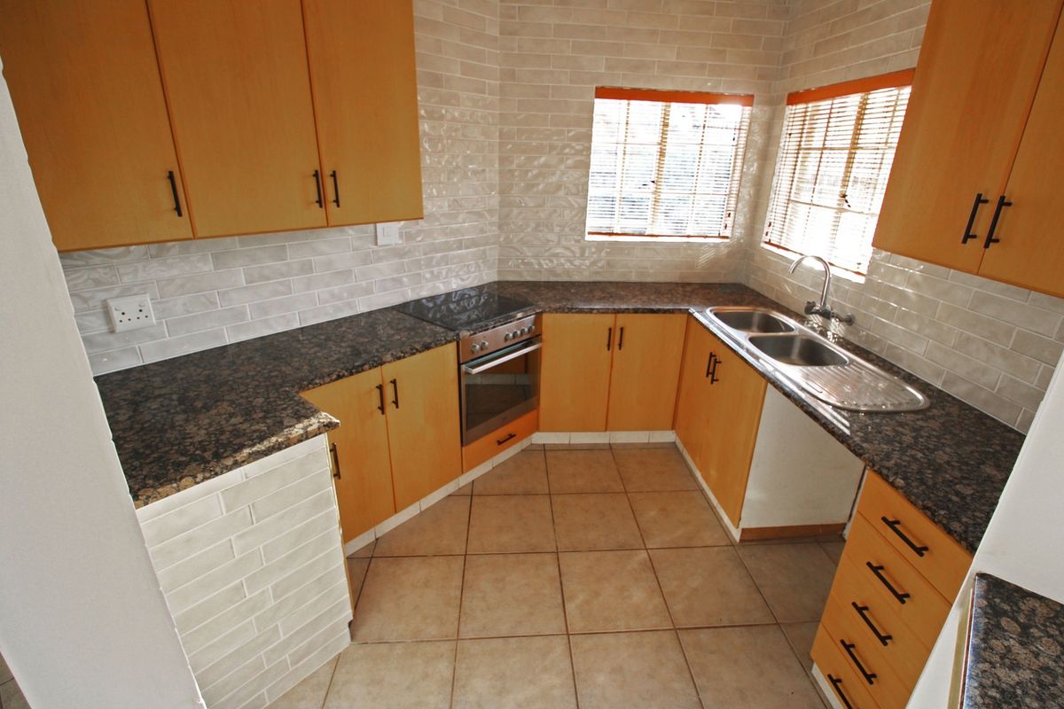 A functional kitchen featuring light wood cabinetry, dark granite countertops, a built-in oven and hob, and a double bowl sink with tiled backsplash.
