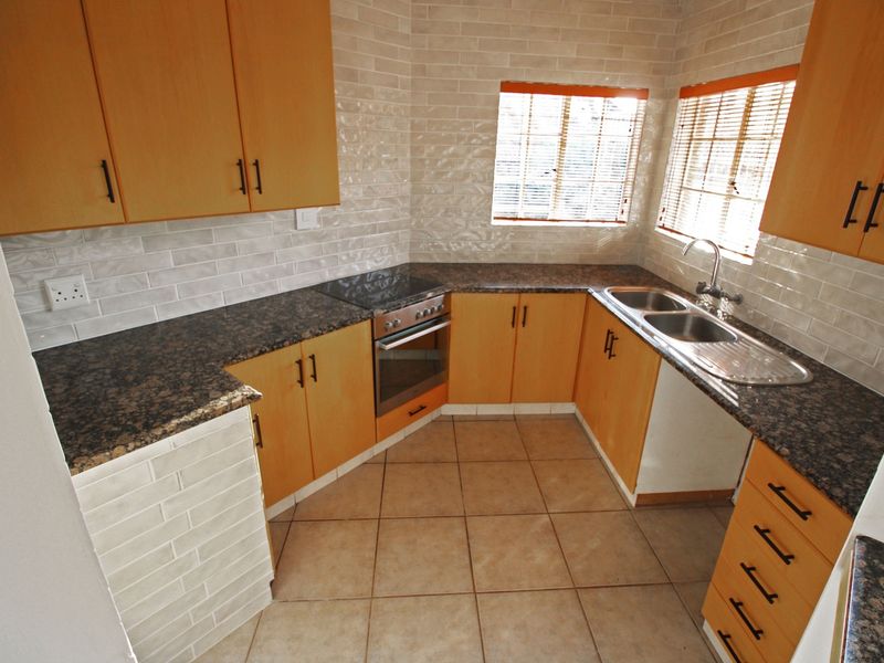 A functional kitchen featuring light wood cabinetry, dark granite countertops, a built-in oven and hob, and a double bowl sink with tiled backsplash.