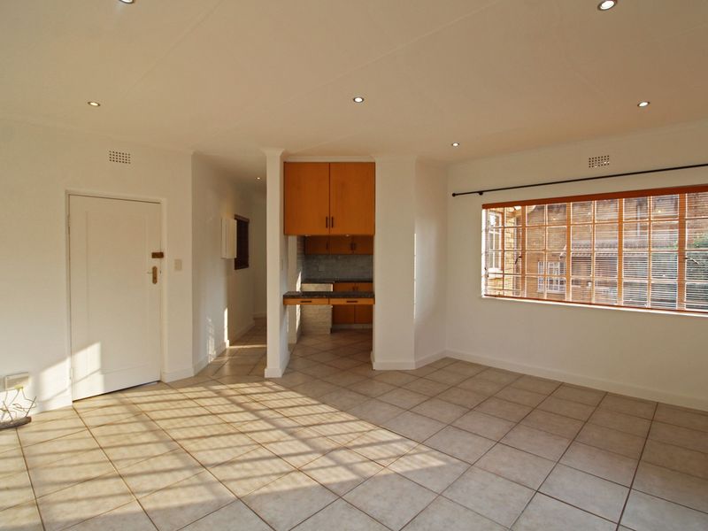 An open-plan living area featuring tiled flooring, recessed lighting, and a compact kitchen nook with built-in cabinetry.