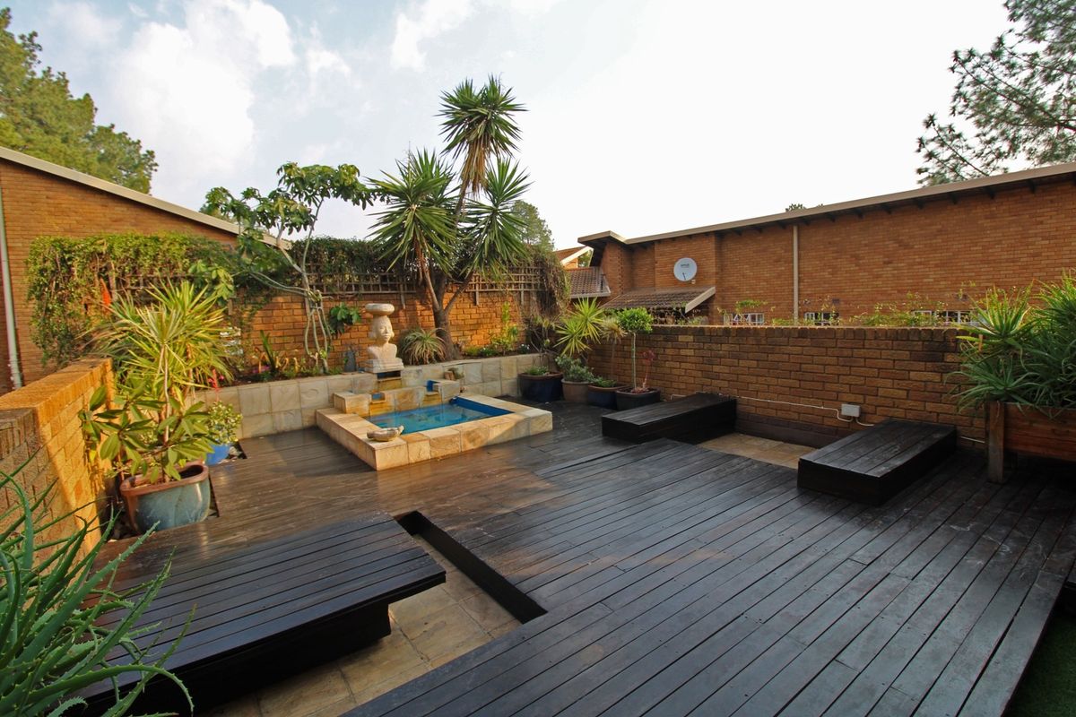 A private rear courtyard featuring timber decking, built-in seating, and a central water feature enclosed by brick boundary walls.
