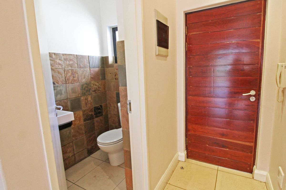 A functional guest bathroom featuring natural stone wall tiling, a toilet, and a wall-mounted basin, adjacent to a solid timber entrance door.