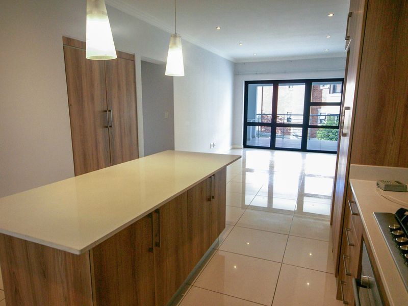 Modern open-plan kitchen featuring a central island with stone countertops, sleek wood-finish cabinetry, gas hob, and tiled flooring leading to a balcony.