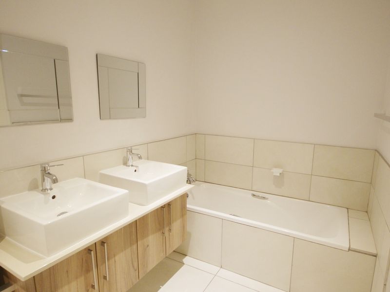 A clean, modern bathroom featuring a double vanity with vessel sinks, a built-in bathtub, and neutral wall tiling.