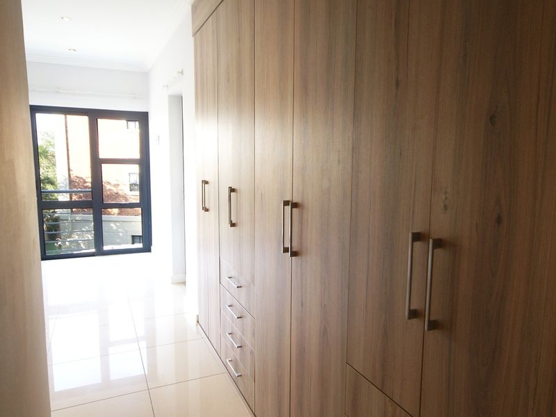 A bright bedroom featuring extensive floor-to-ceiling built-in wooden cupboards, polished tile flooring, and a large window providing natural light.