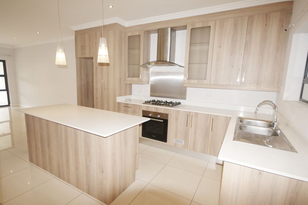 Modern kitchen featuring light wood-grain cabinetry, stone countertops, a central island, and integrated stainless steel appliances, finished with sleek tiled flooring.