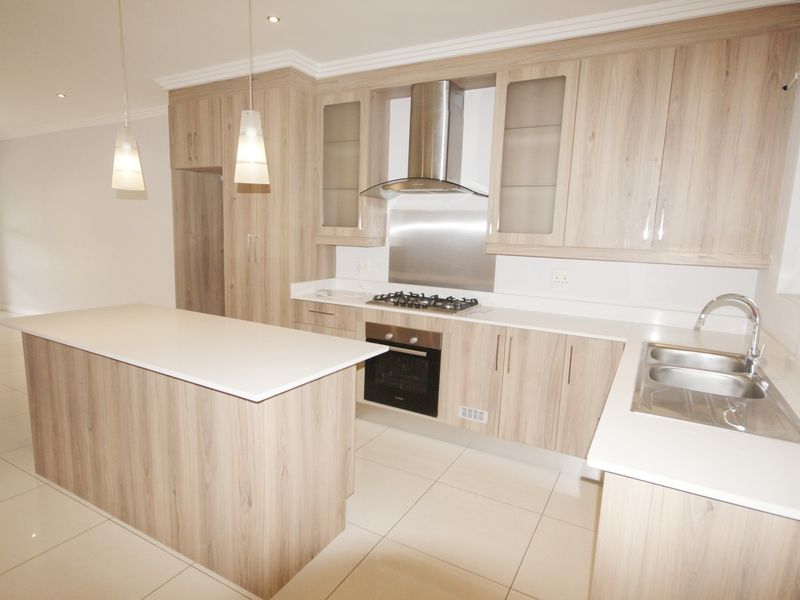 Modern kitchen featuring light wood-grain cabinetry, stone countertops, a central island, and integrated stainless steel appliances, finished with sleek tiled flooring.