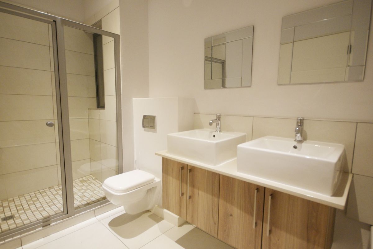 Modern bathroom featuring a double vanity with vessel sinks, wall-mounted toilet, and a glass-enclosed shower with neutral tiling.