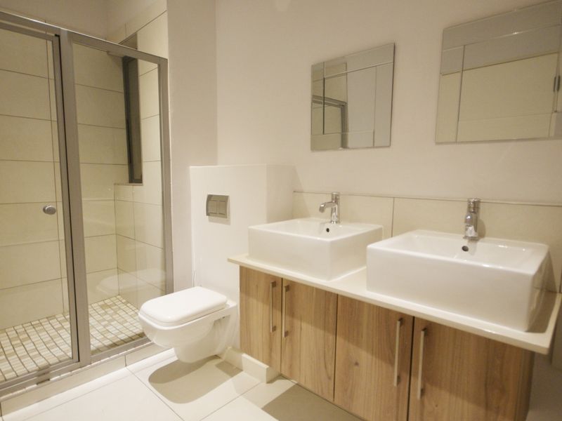 Modern bathroom featuring a double vanity with vessel sinks, wall-mounted toilet, and a glass-enclosed shower with neutral tiling.