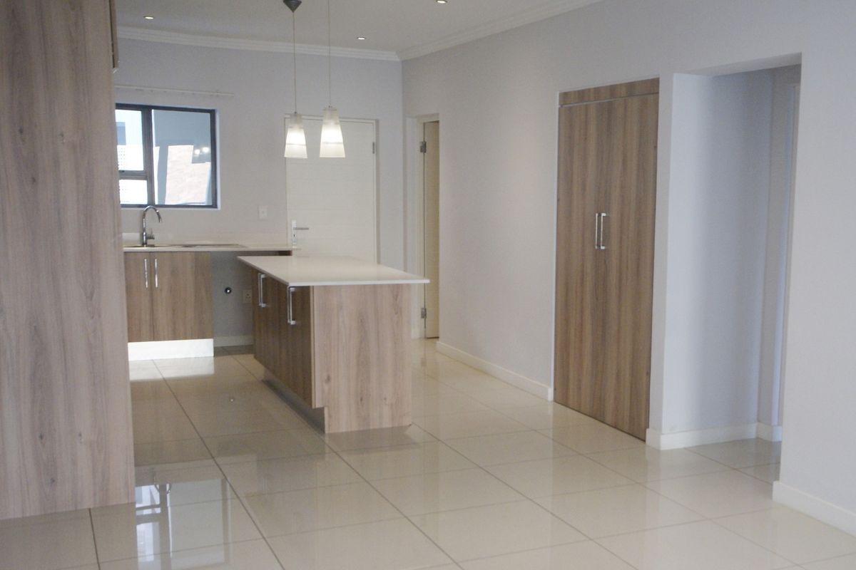 Modern open-plan kitchen area featuring a central island, sleek wood-finish cabinetry, recessed lighting, and polished tiled flooring in a clean, vacant space.
