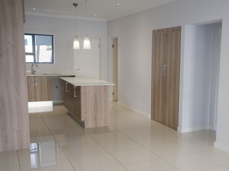 Modern open-plan kitchen area featuring a central island, sleek wood-finish cabinetry, recessed lighting, and polished tiled flooring in a clean, vacant space.