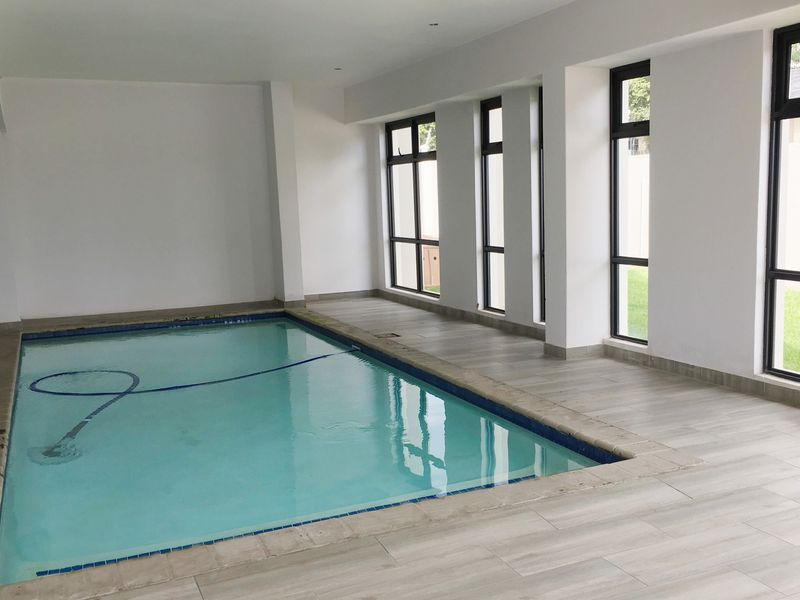 An indoor swimming pool area featuring large windows, neutral tiled flooring, and clean white walls, offering a bright and spacious environment.